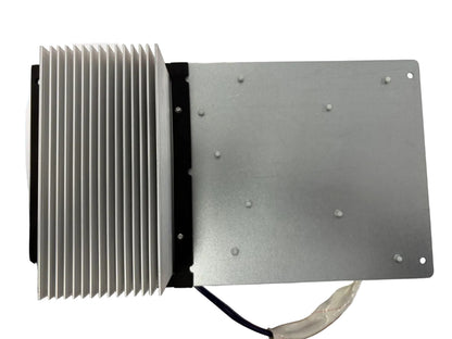 A silver metal electronic heatsink and mounting plate assembly with attached wires, photographed from above on a white sheet over a wooden surface.